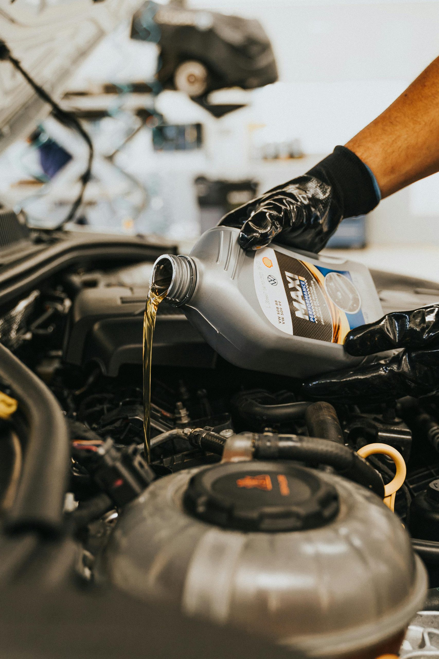 A close-up of a mechanic in gloves pouring engine oil into a car engine, showcasing automotive maintenance.